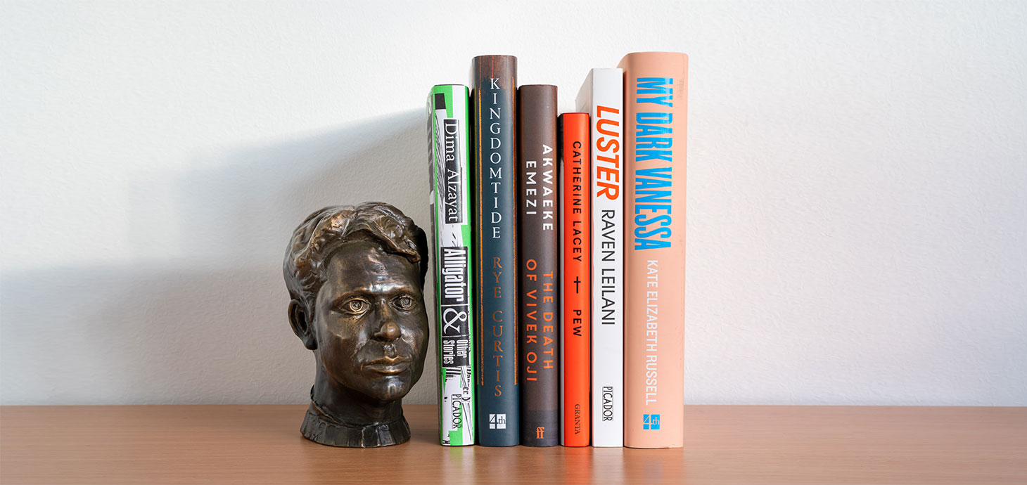 The six shortlisted books on a shelf next to a bust of Dylan Thomas