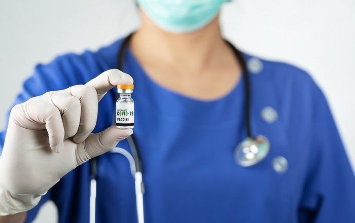Doctor holding a vial of vaccine; new research finds that no cases of a rare blood disorder have been identified in the COVID-19 vaccinated population of Wales.