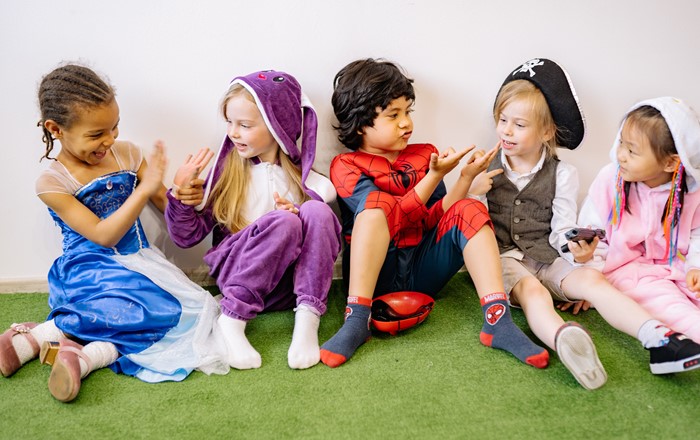 Group of five young children, wearing fancy dress sitting on a carpet playing and laughing together