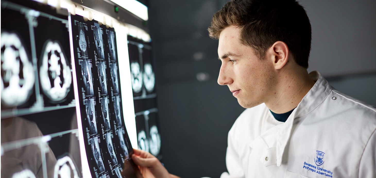 Male medical student wearing white coat looking at scan  images on a light box