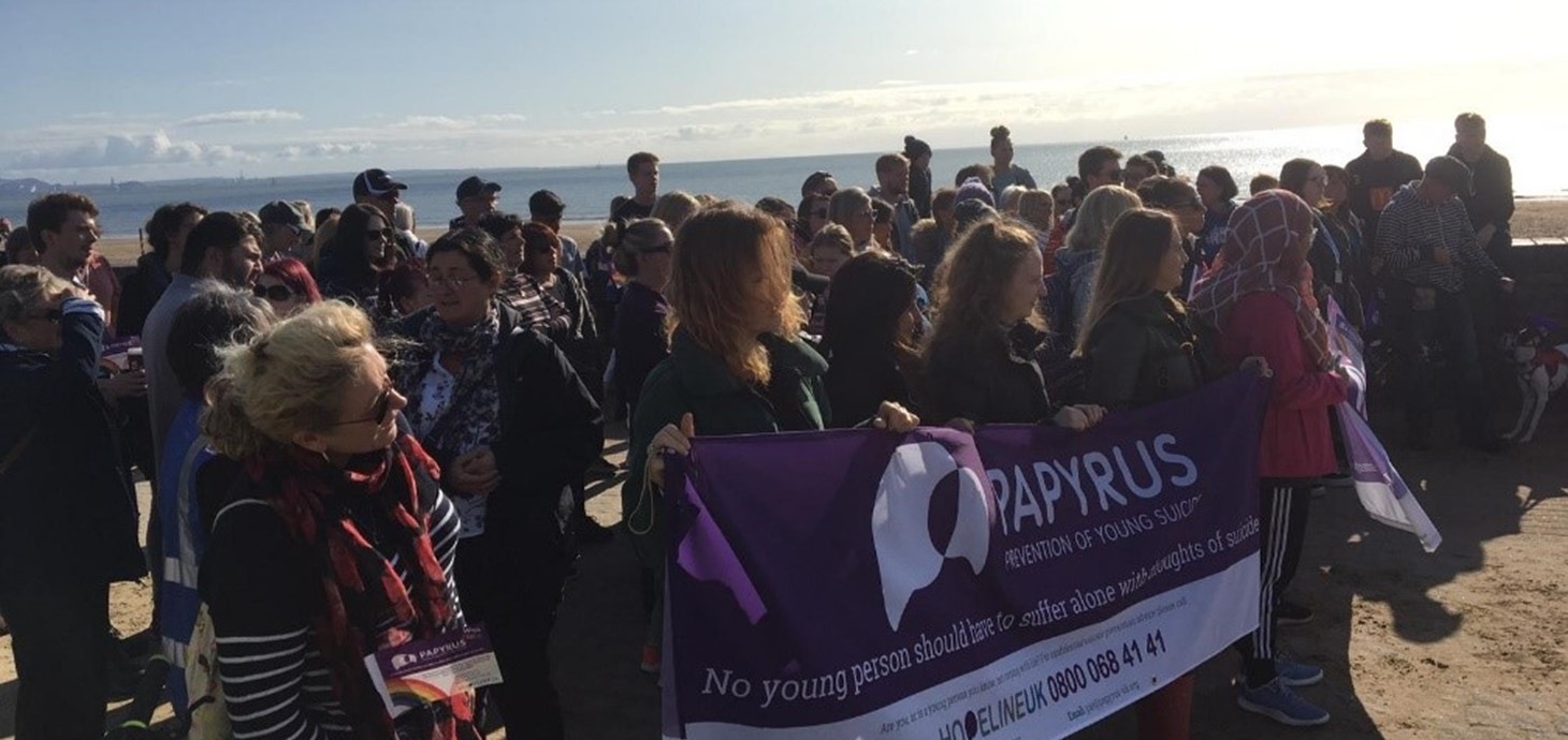 Group of people standing on a beach near the sea, holding up a banner