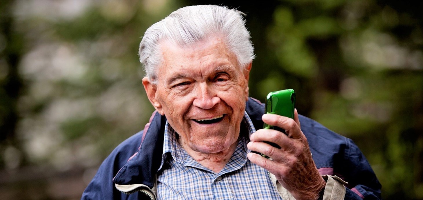 An older man holding a mobile phone and smiling