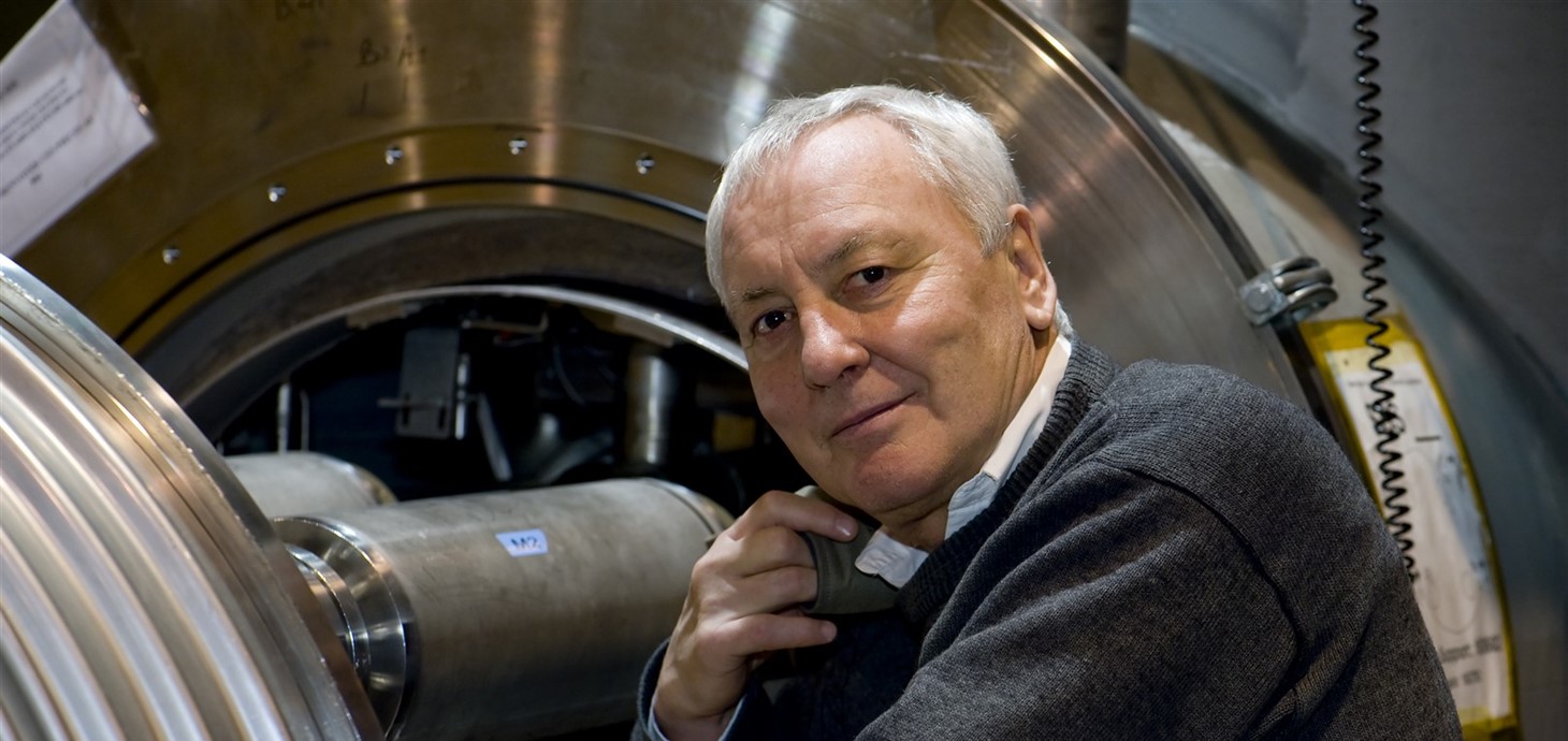 A photo of Professor Lyn Evans standing next to the Large Hadron Collider.