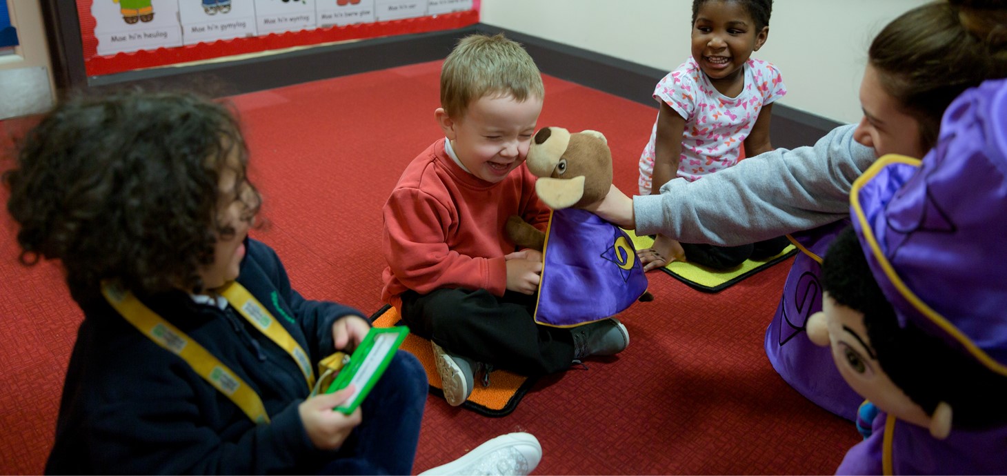Laughing children play with Doti and Dewin cuddly toys at a Mudiad Meithrin playgroup. 