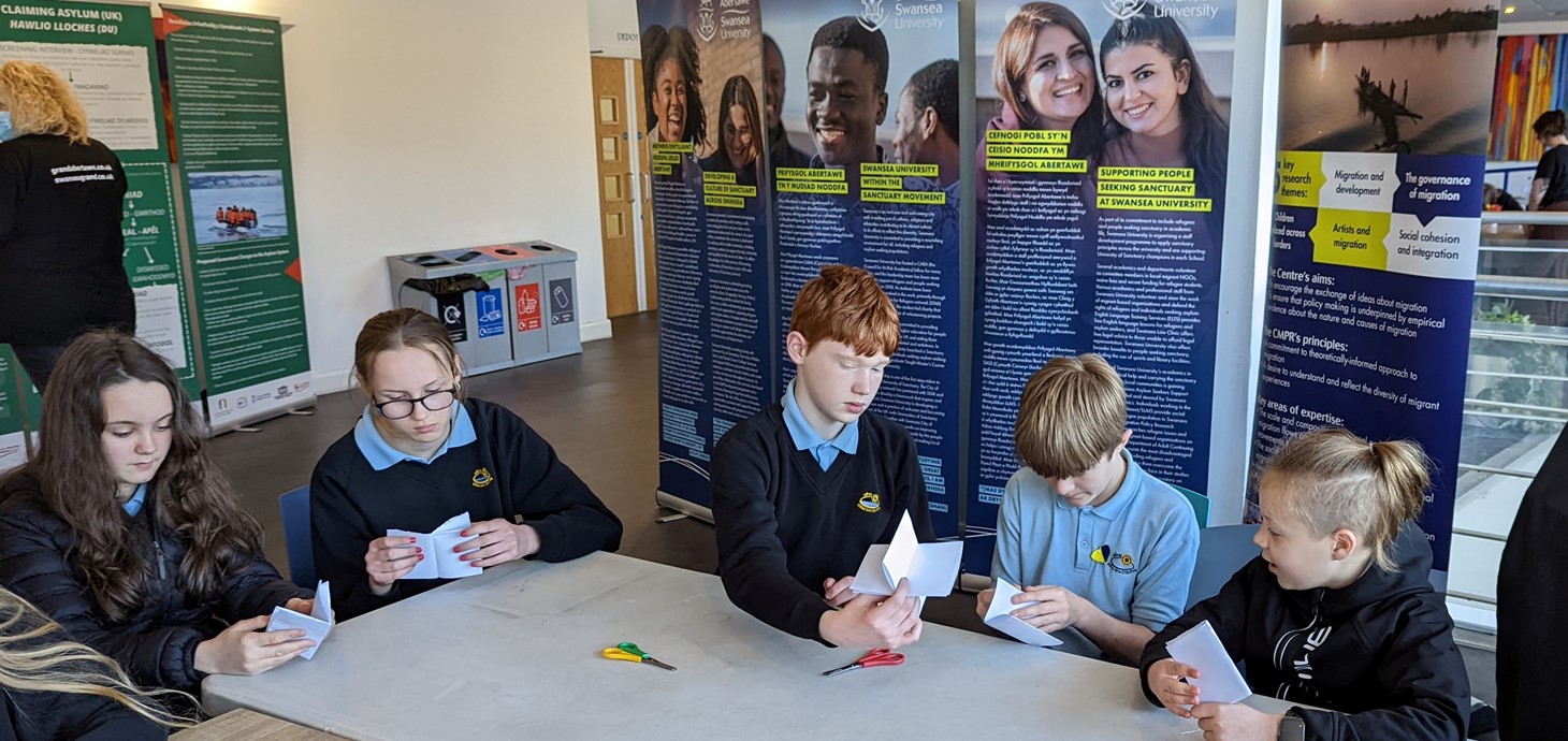 Five school pupils in uniform sitting at a table making things with paper and scissors. Behind them are information panels.
Pupils from Ysgol Gyfun Gŵyr in Gowerton taking part in activities at one of the University’s workshops at the exhibition. 