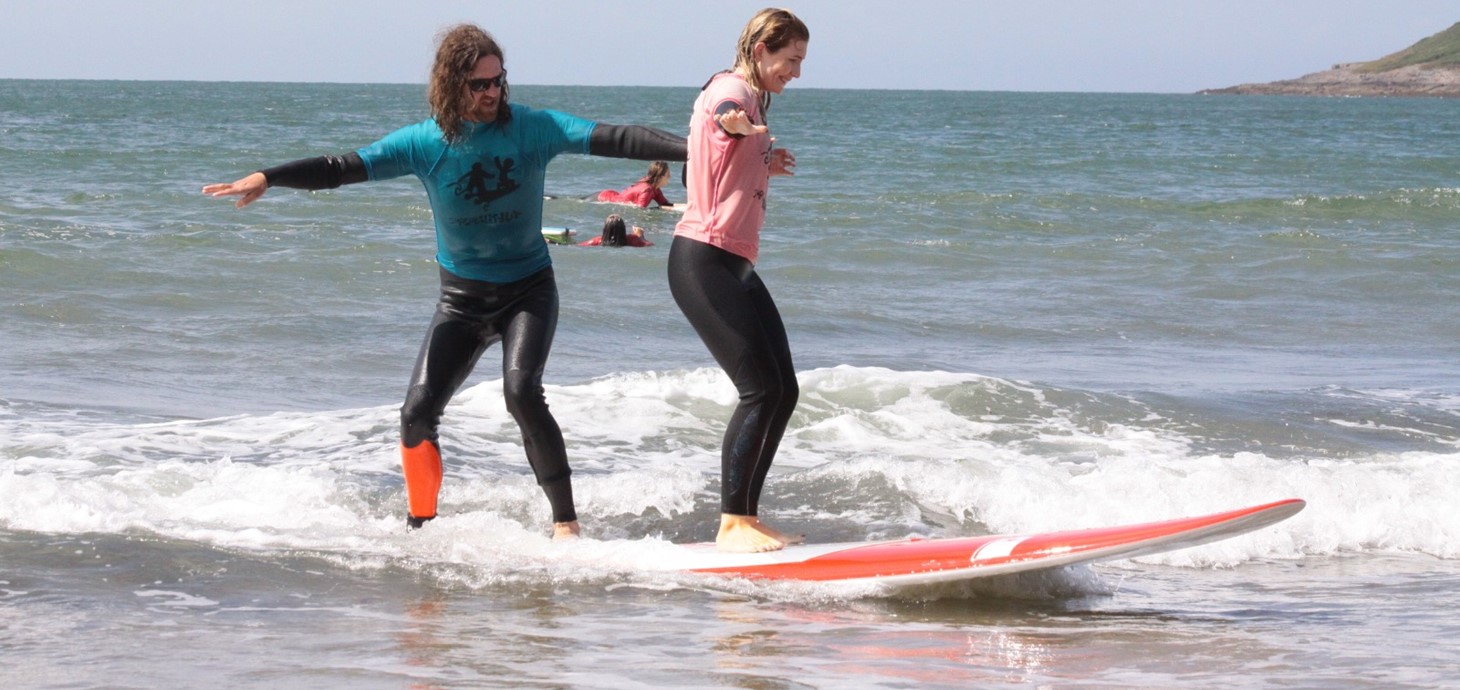 Man and woman in wetsuits standing up on a surfboard in the sea