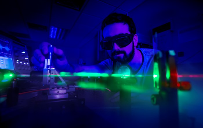 Scientist wearing goggles conducting an experiment using a laser in a darkened room