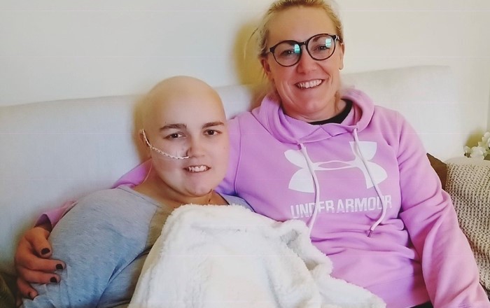 Teenage female cancer patient sitting alongside a smiling woman 