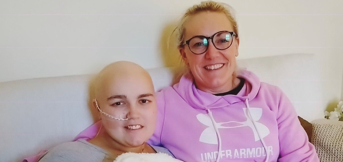 Teenage female cancer patient sitting alongside a smiling woman 