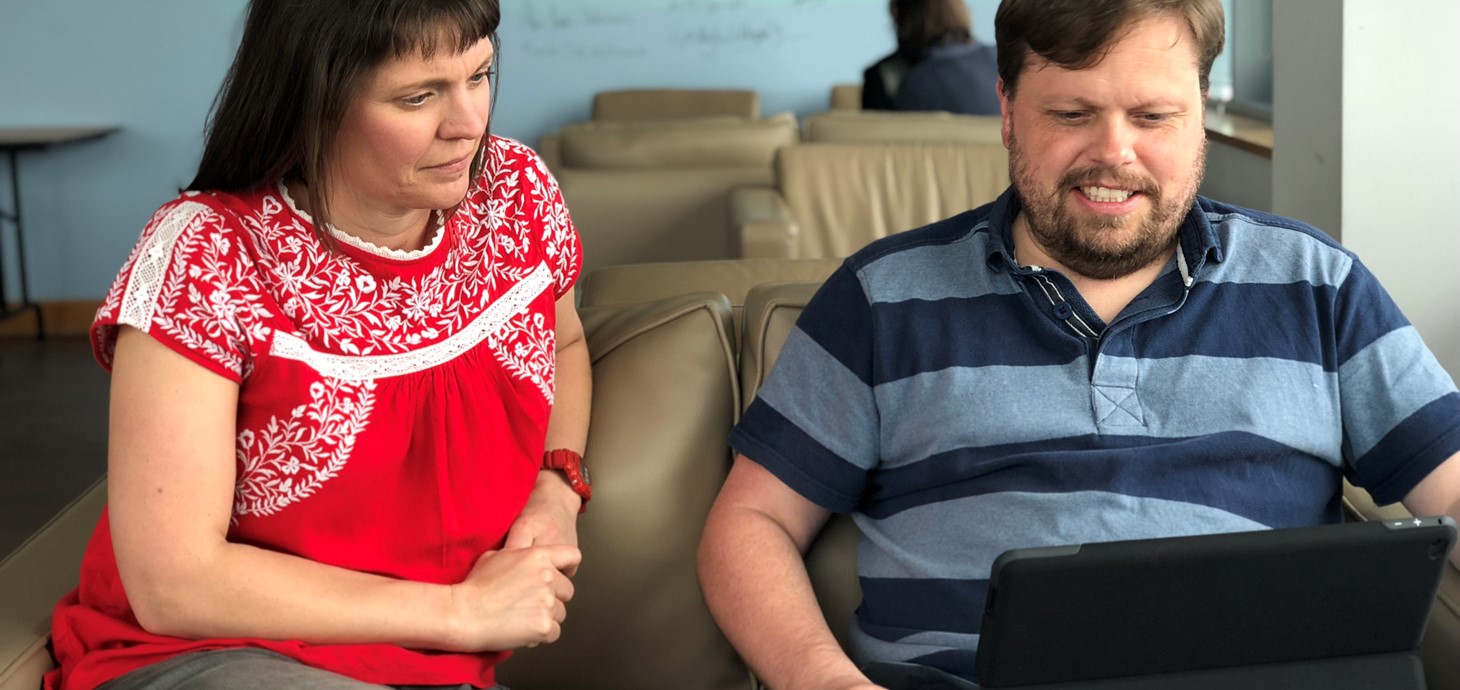 Man and woman sitting on a sofa looking at a laptop being held by the man.