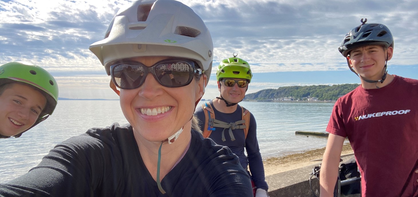 Four people wearing cycling helmet smiling at the camera with the sea in the background