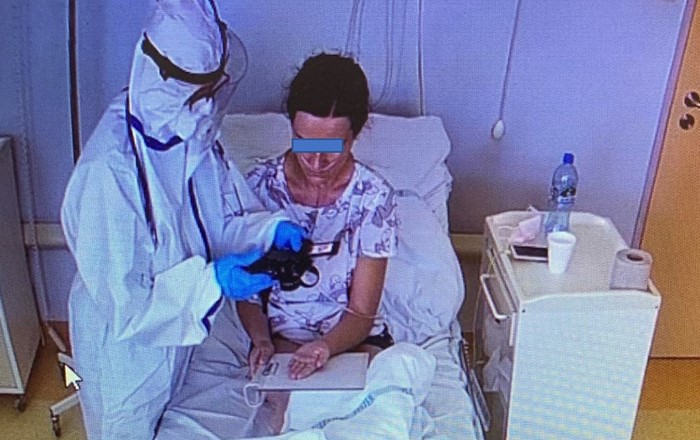 Anonymous patient sitting in bed having hands photographed by person wearing full PPE