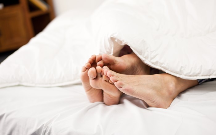 A pair of men's and women's feet sticking out at the end of a white duvet