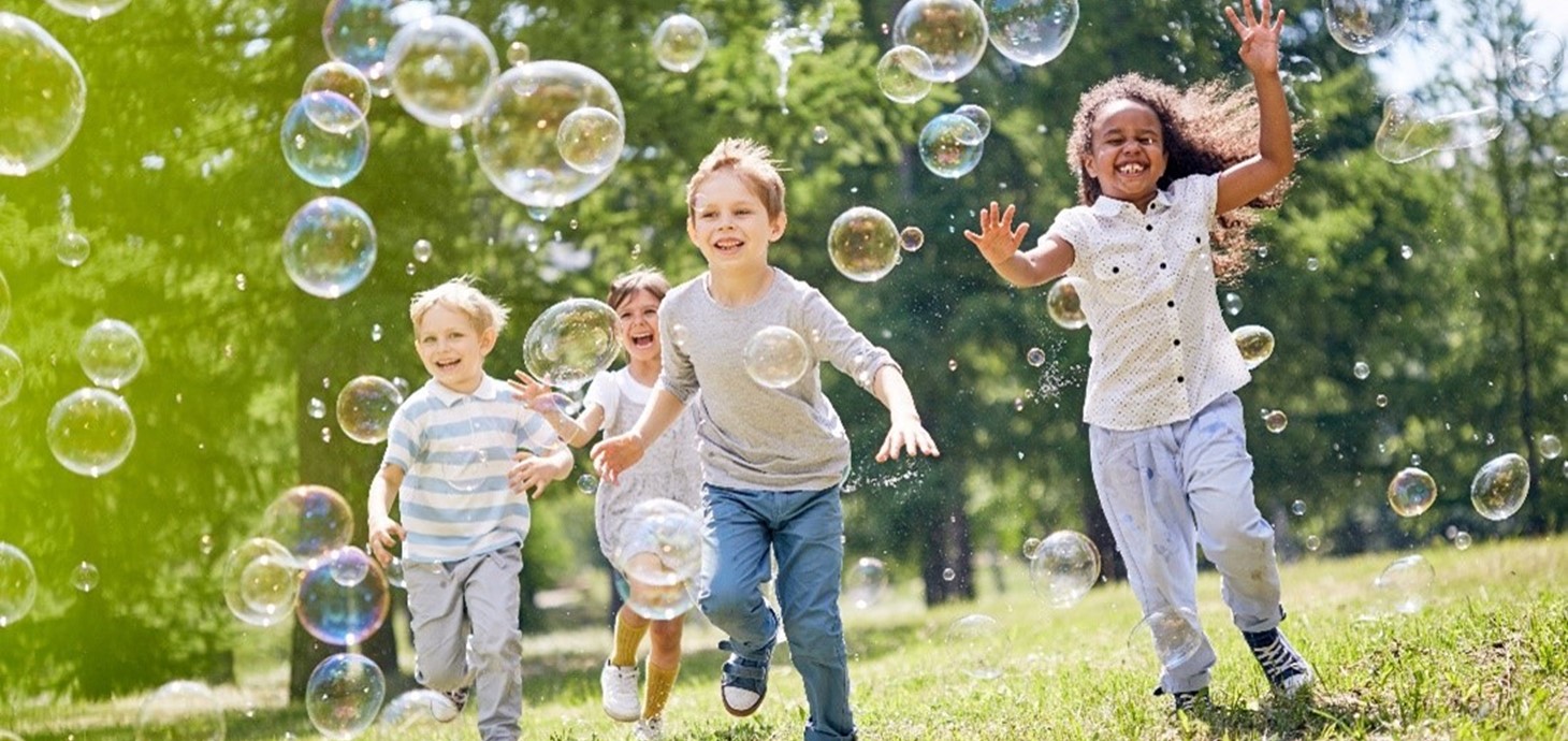 Smiling children running across grass chasing bubbles