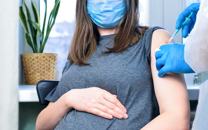 Pregnant woman wearing face mask receiving a vaccination 