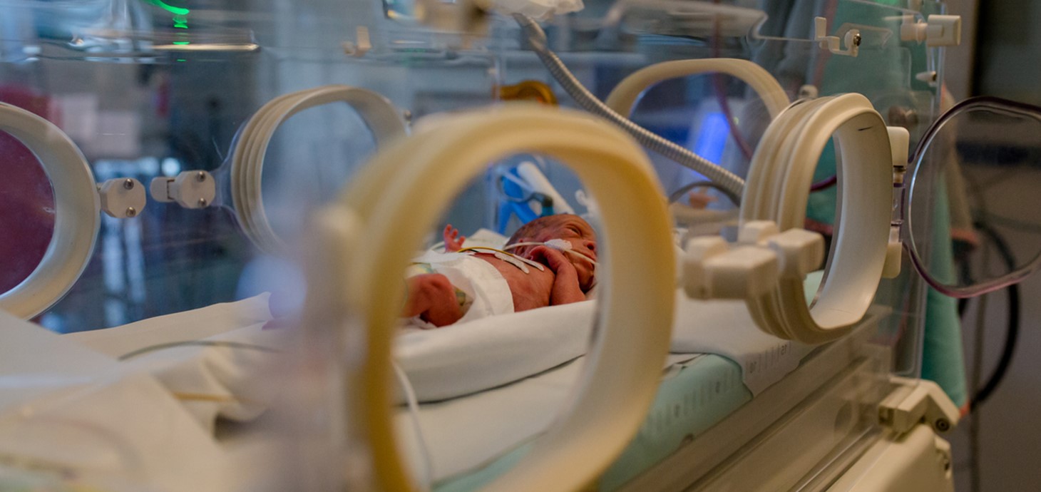 Premature baby in nappy seen through door of incubator in special care baby unit 