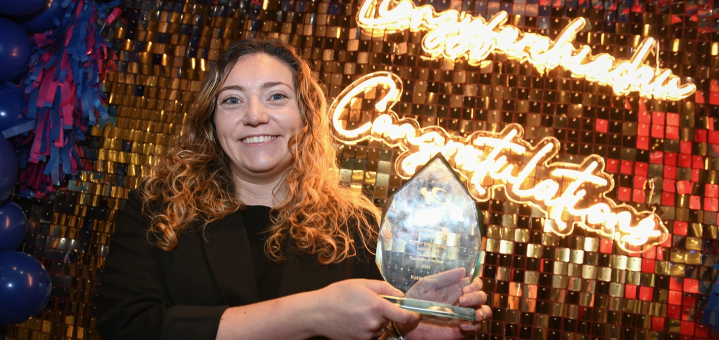 Katie Harris holds her award in front of a light-up sign that says ‘Congratulations’.