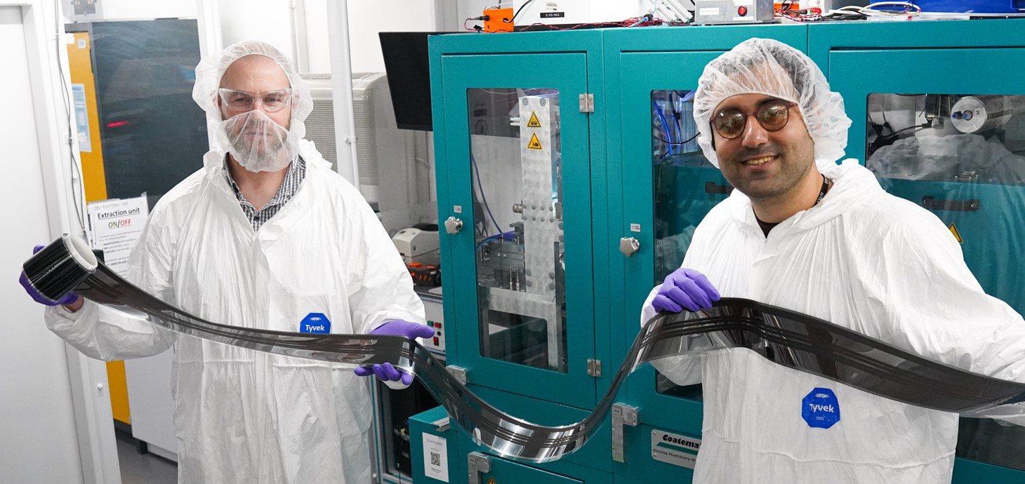Dr David Beynon (Left) and Dr Ershad Parvazian (Right) wearing protective clothing and holding a sample of the new fully roll-to-roll (R2R) coated device.