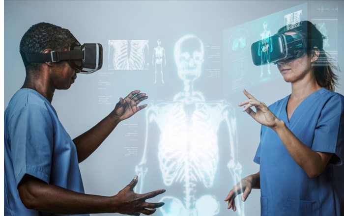 Two people in medical scrubs wearing VR headsets by an image of a skeleton