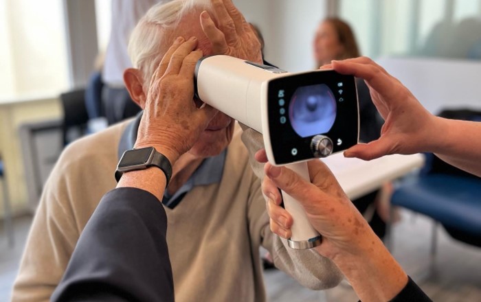Elderly man having eye tested using handheld camera