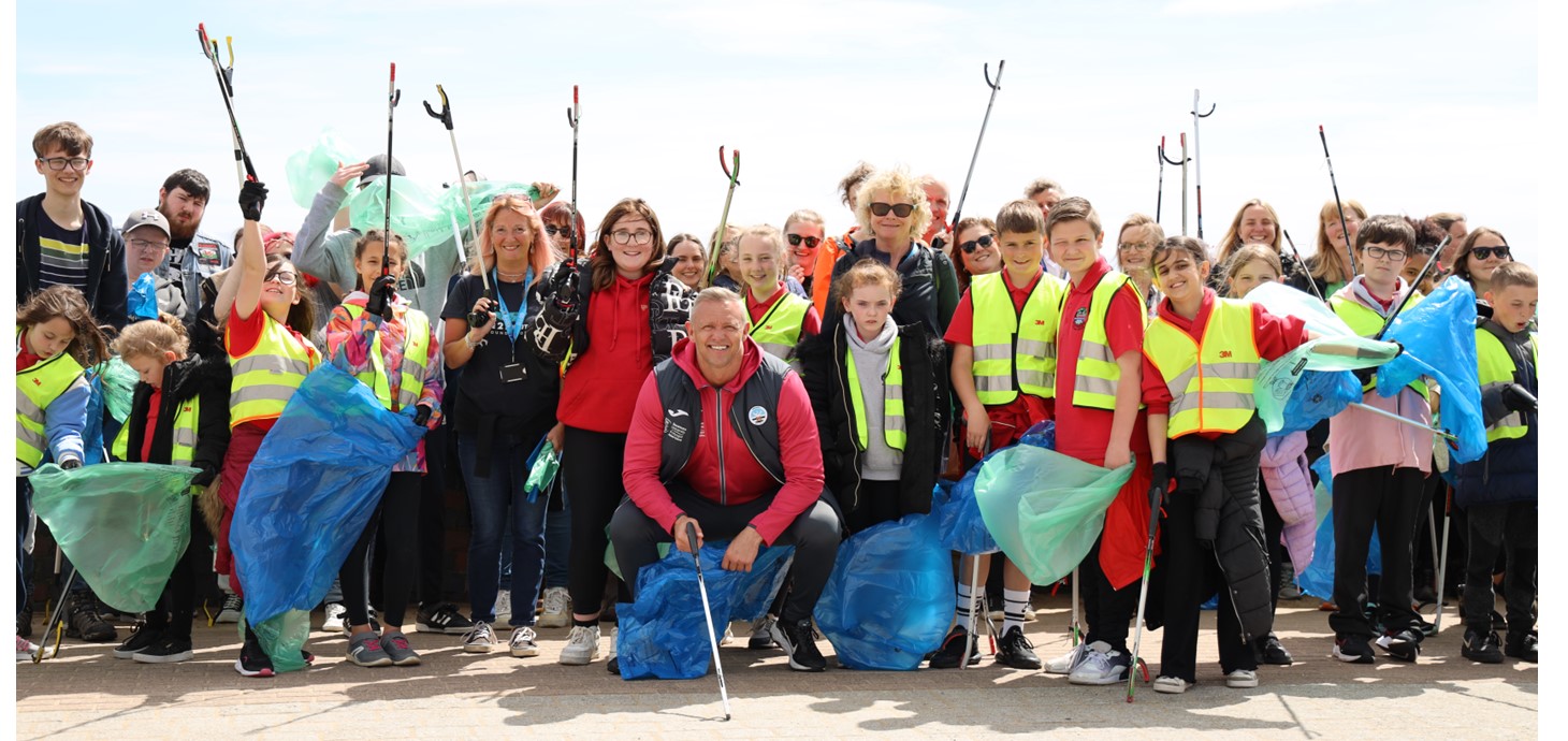 Group of children and adults outside waving litter grabbers and holding refuse bags