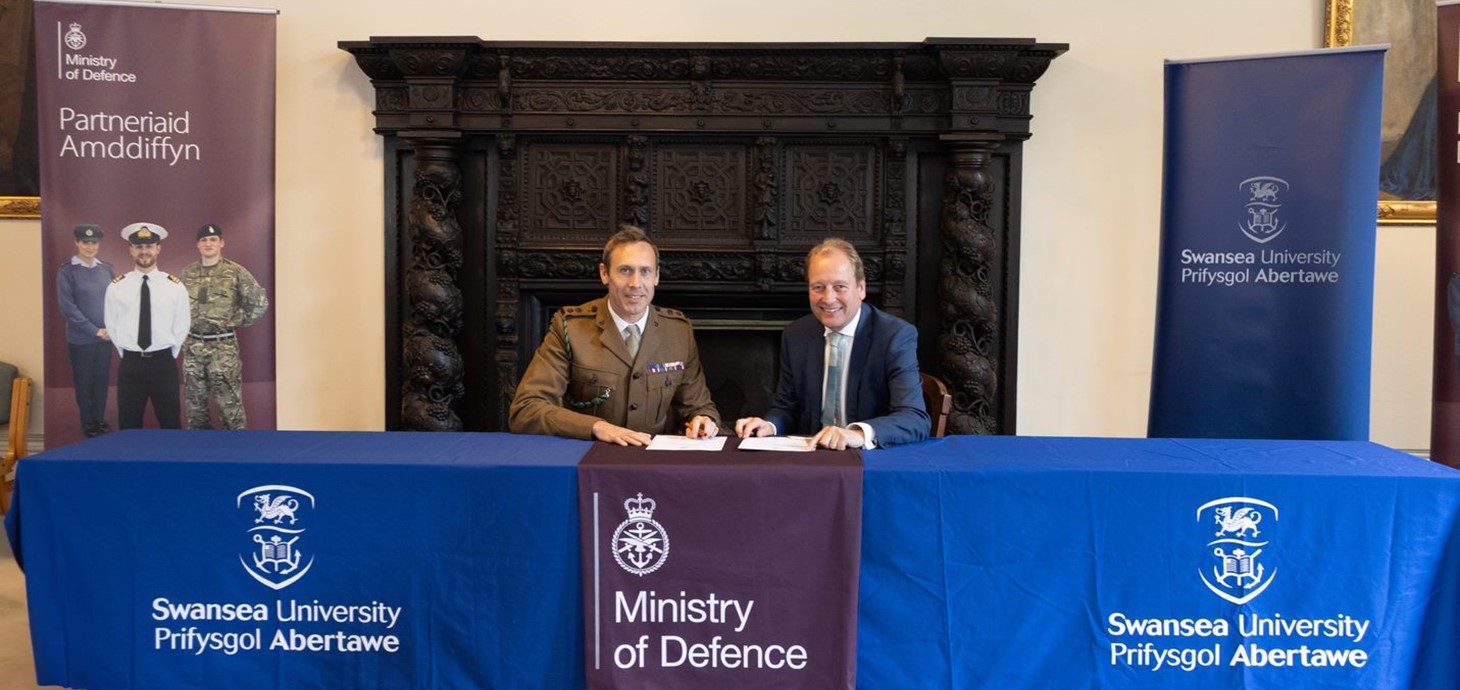 The Commanding Officer of the Wales Universities Officers’ Training Corps, Lieutenant Colonel Andrew Child pictured sitting in front of a large fireplace signing the Armed Forces Covenant with Professor Paul Boyle, Vice-Chancellor of Swansea University. 