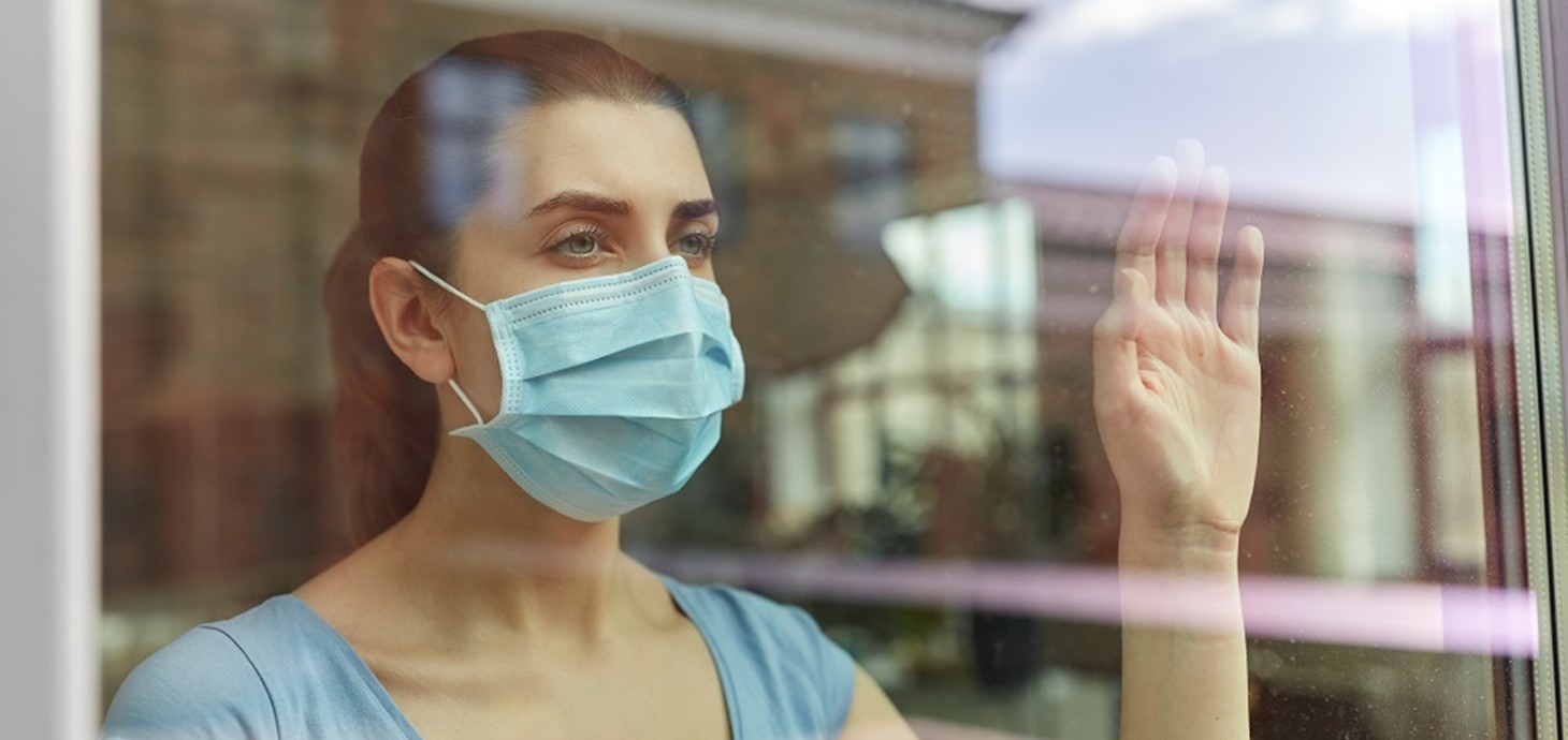 A woman wearing a face mask looking out a window
