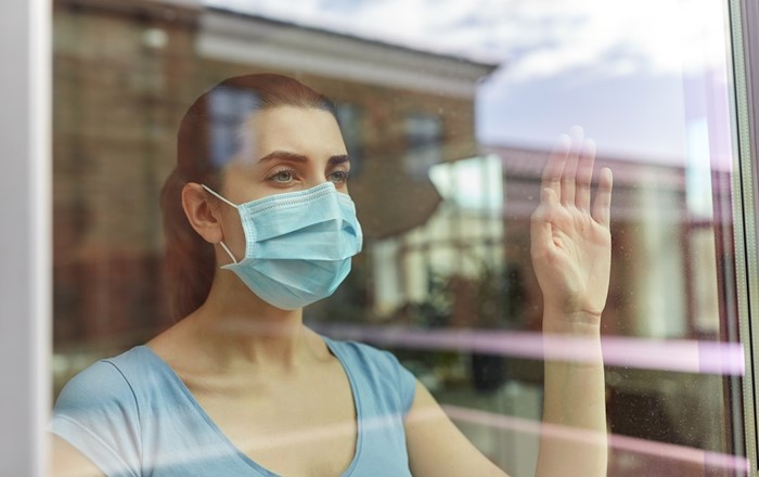 A woman wearing a face mask looking out a window