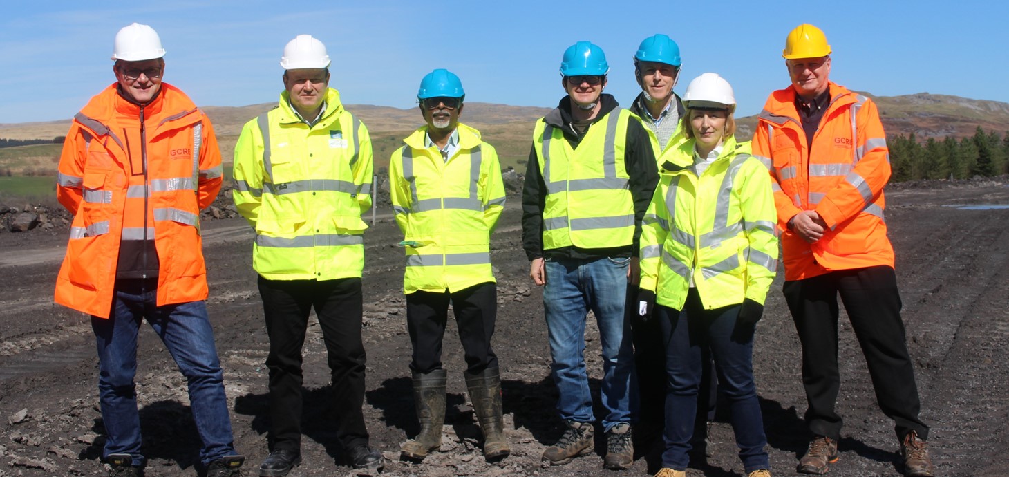 Seven people wearing high-viz jackets and hard hats standing outside on a hilltop site