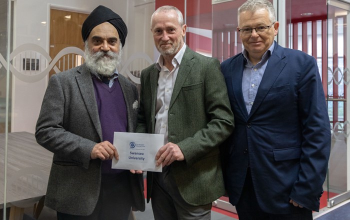 Three men standing indoors holding a cheque