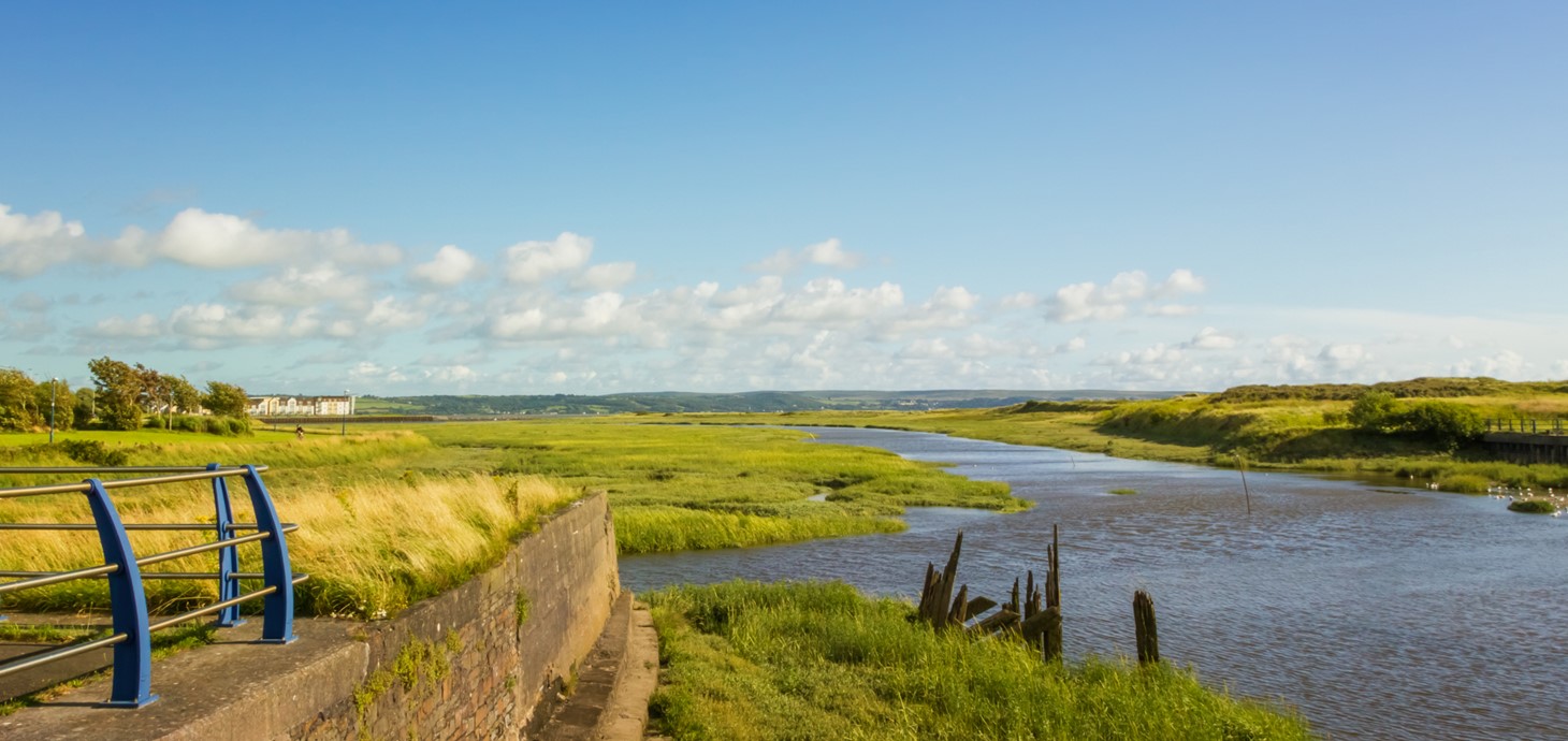 View across an estuary surrounded by marshes with a wall and railings