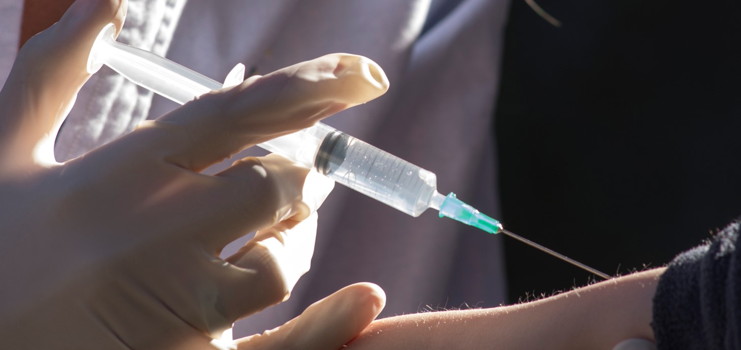 Close-up image of hand holding a syringe injecting someone in the arm