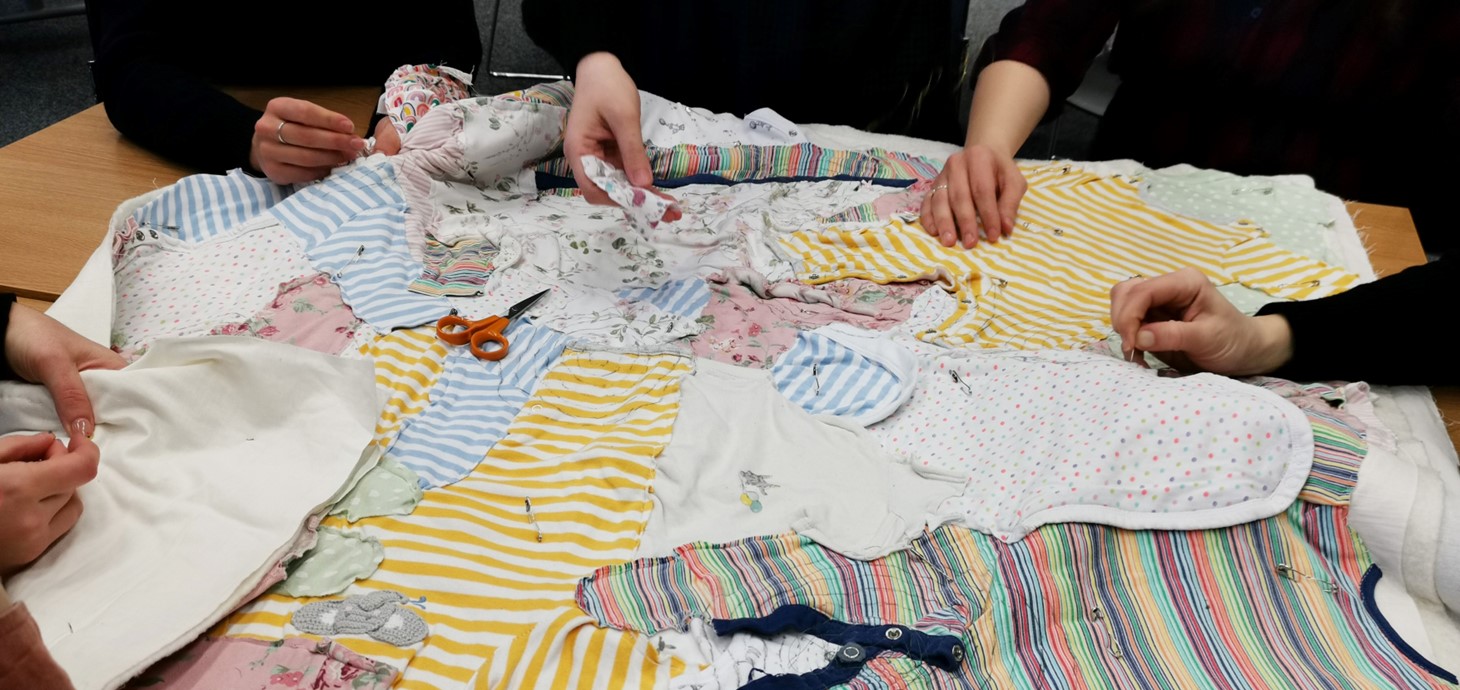 Women's hands sewing pieces of a quilt made of baby clothing