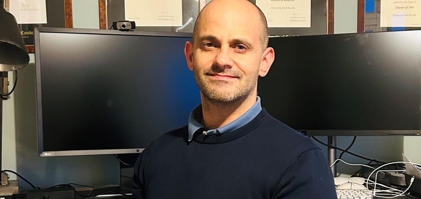 White man looking at camera in front of two computer screens.