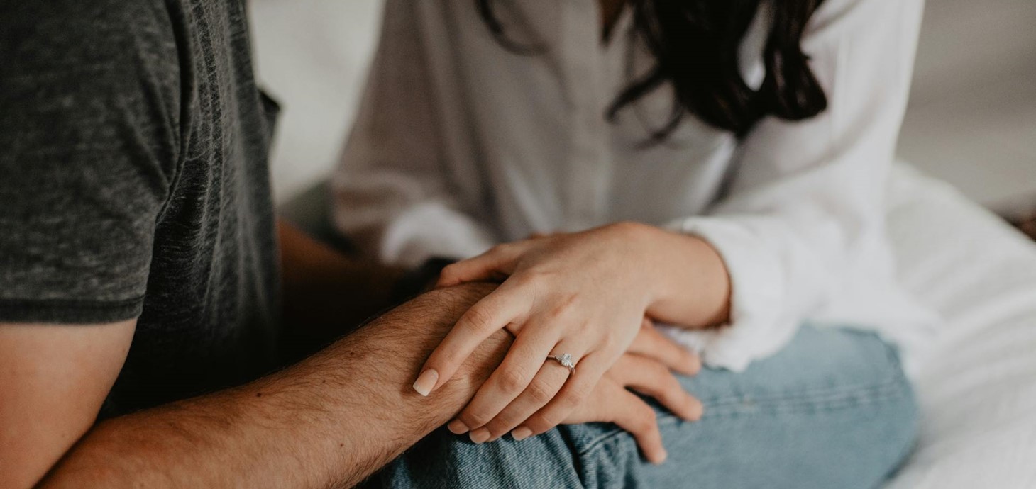 A man and woman holding hands; the woman is wearing an engagement ring. 
