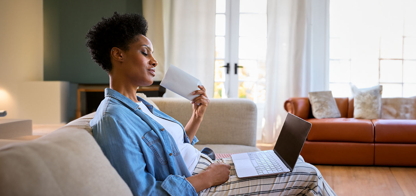 A menopausal mature woman at home looking at a laptop while having a hot flush and fanning herself.