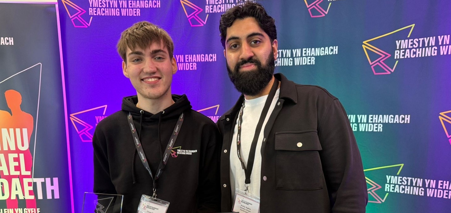 Two young men standing together in front of banner