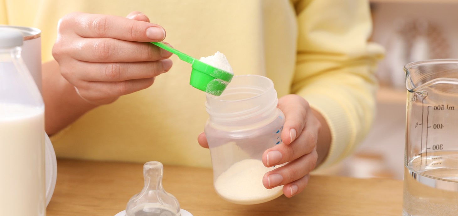 A close-up of a woman preparing a bottle of infant formula milk