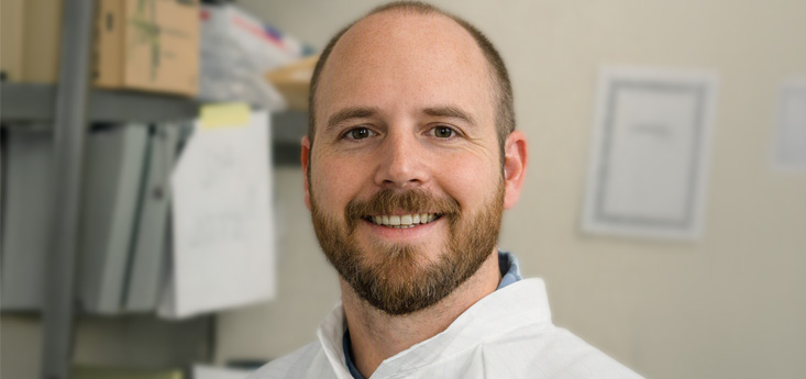 Head and shoulders image of a man wearing a white coat in a laboratory.