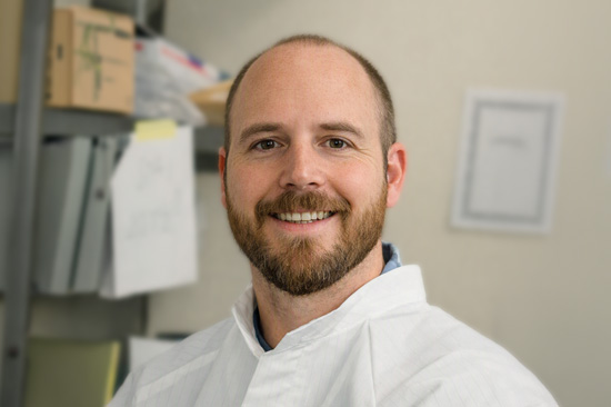 Head and shoulders image of a man wearing a white coat in a laboratory.