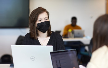 A group of students studying, with a female student in the foreground wearing a face mask