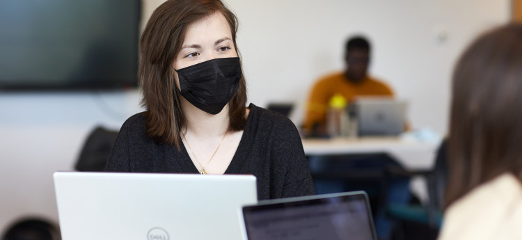A group of students studying, with a female student in the foreground wearing a face mask