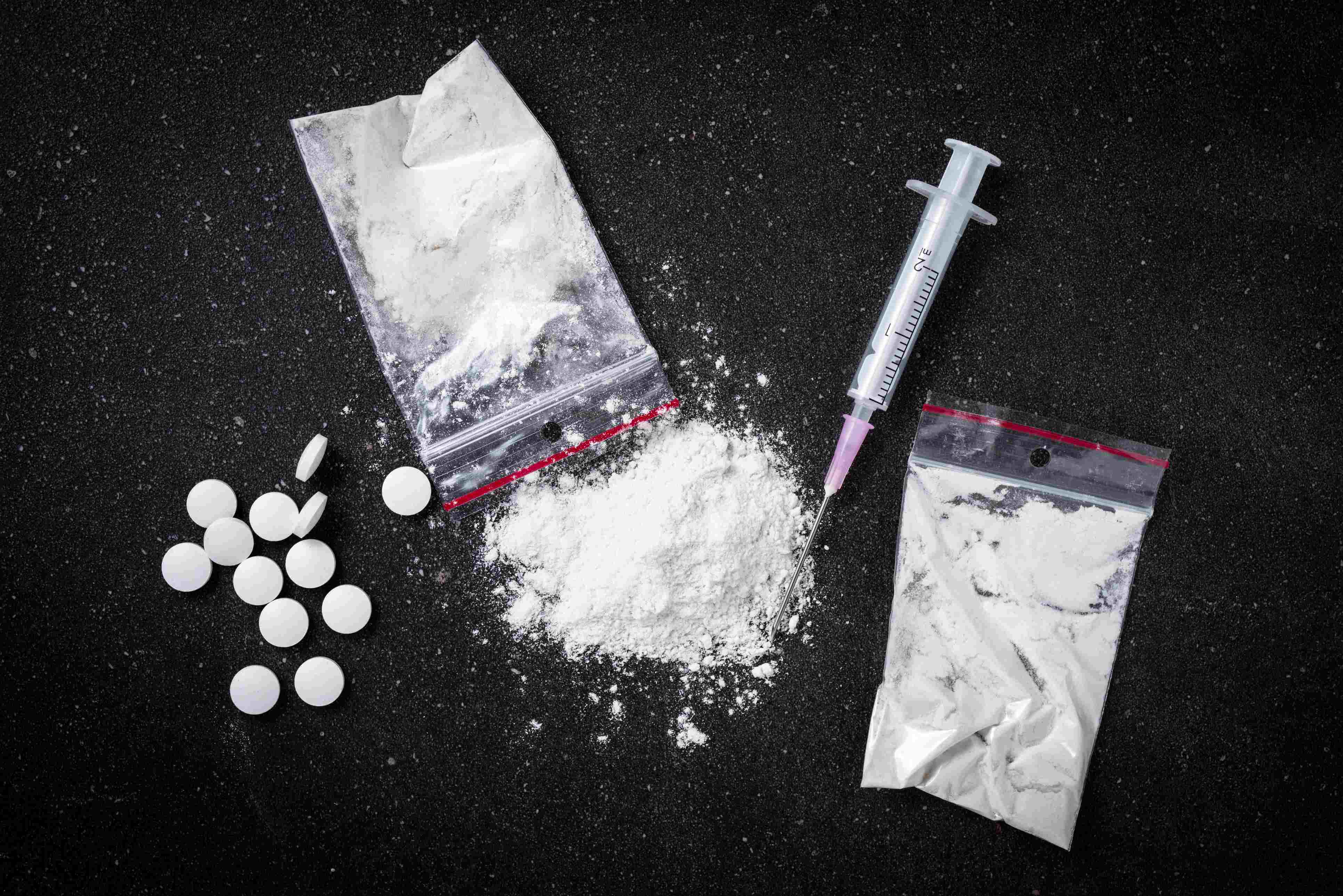 Scattered pills, white powder in a transparent plastic bag and a syringe 