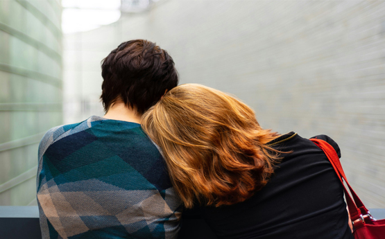 A photo from behind of a woman resting her head on a man's shoulder