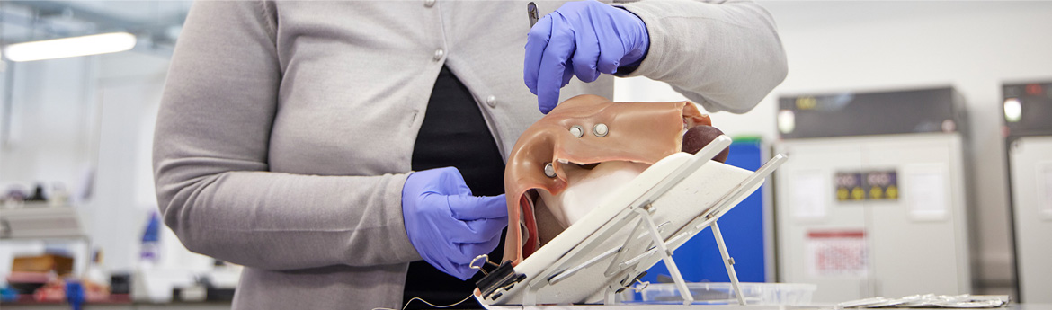 A person wearing gloves with a scalpel practicing on a hyper-realistic training model