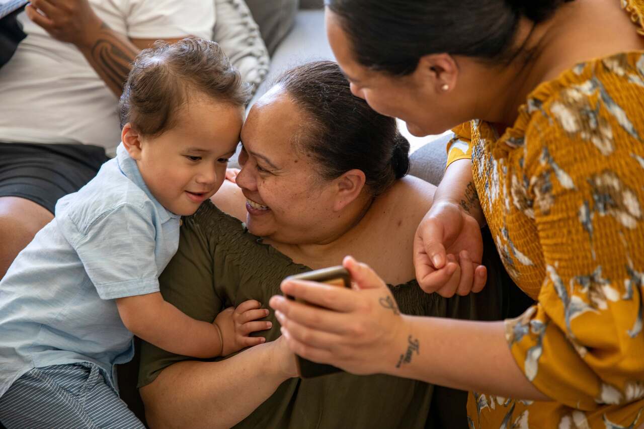 Two women showing a child something on a phone. 