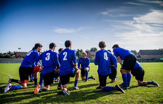 A football team huddle on the ground to receive a brief from the coach