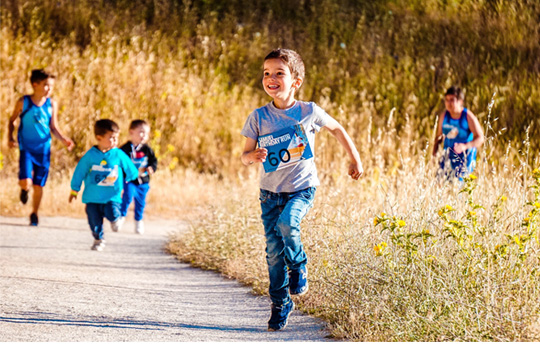 A small boy runs with his friends in a path amongst fields