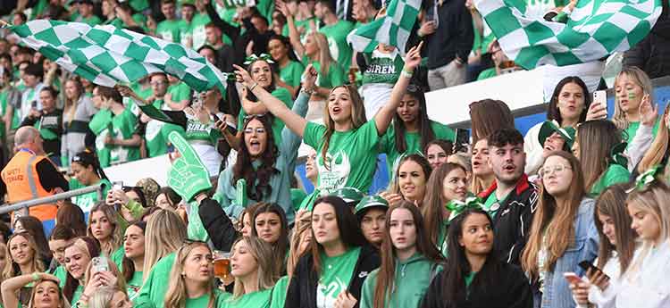 Students dressed in green celebrating in stands at swansea.com stadium