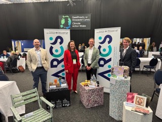 4 people from the ARCS team stand by banners and examples like a plastic chair